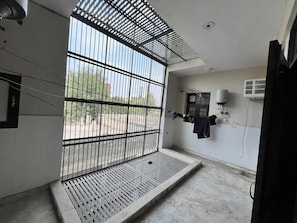 Una habitación con una ventana con barrotes, un banco pequeño y un equipo de aire acondicionado fijado a la pared.