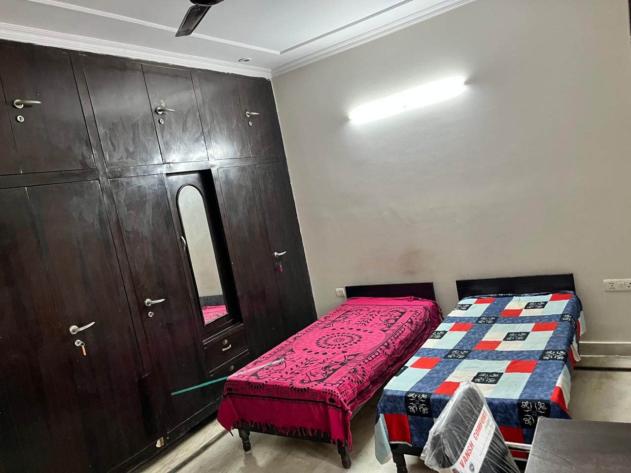 A room with a wardrobe, a bed with a patterned bedspread, and a mirror.