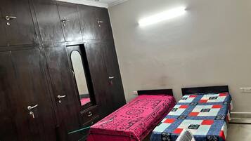 A room with a wardrobe, a bed with a patterned bedspread, and a mirror.