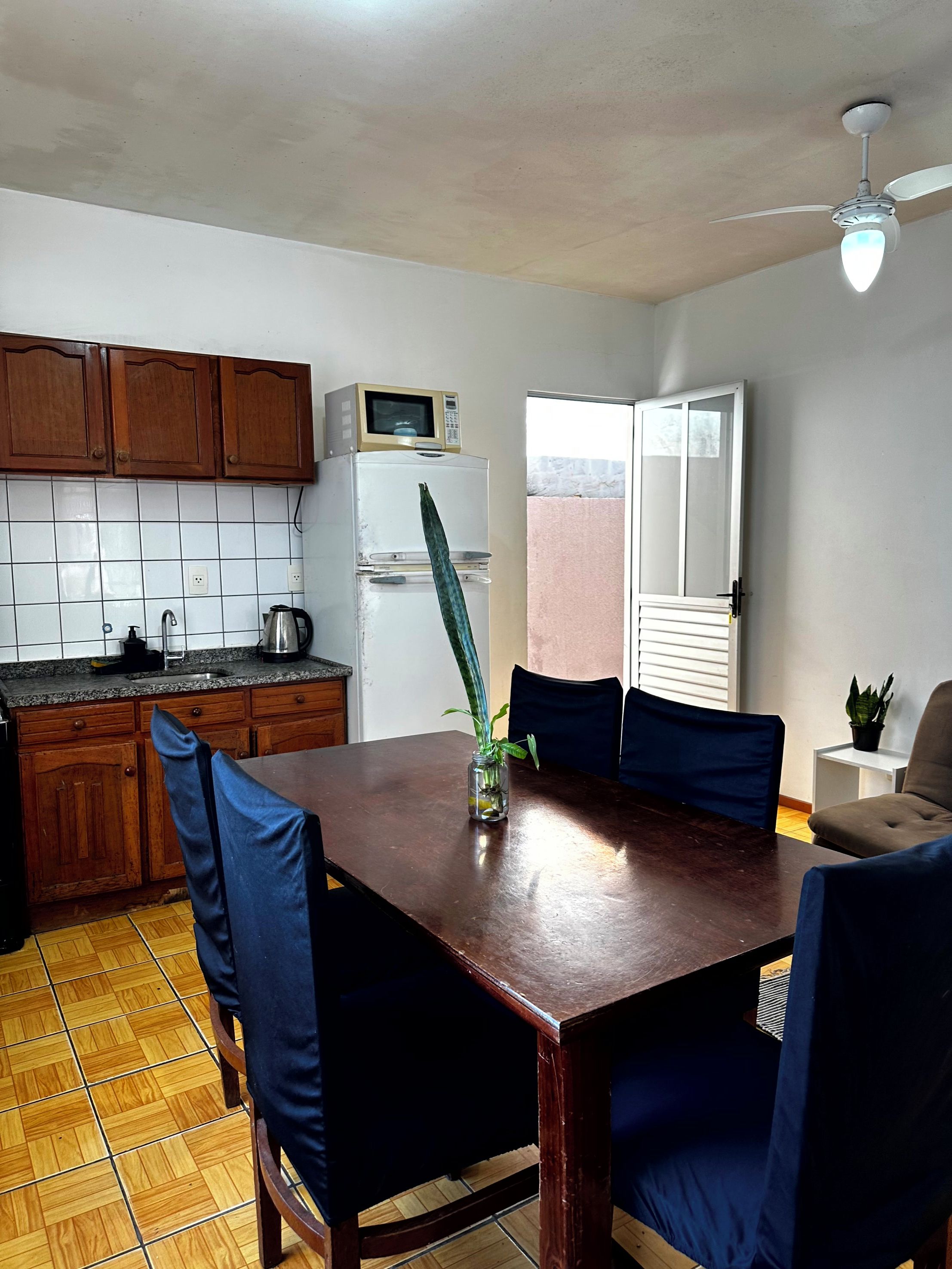 A kitchen with wooden cabinets, a white refrigerator, a microwave, and a dining table with blue chairs.