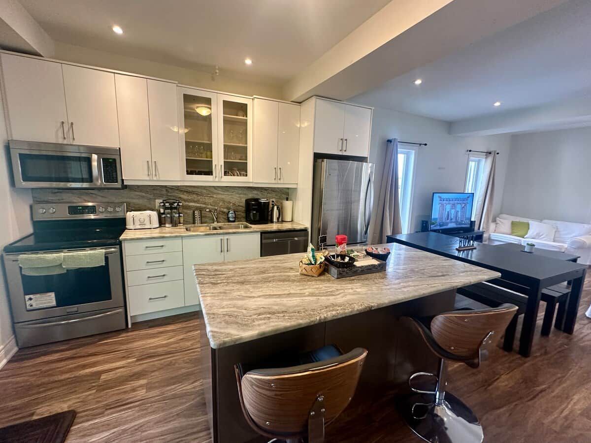 A modern kitchen with white cabinets, a central island, and a dining area with a TV.