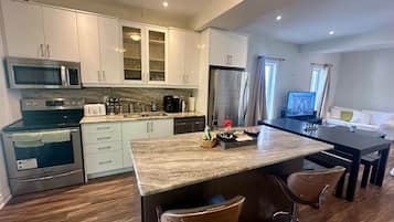A modern kitchen with white cabinets, a central island, and a dining area with a TV.