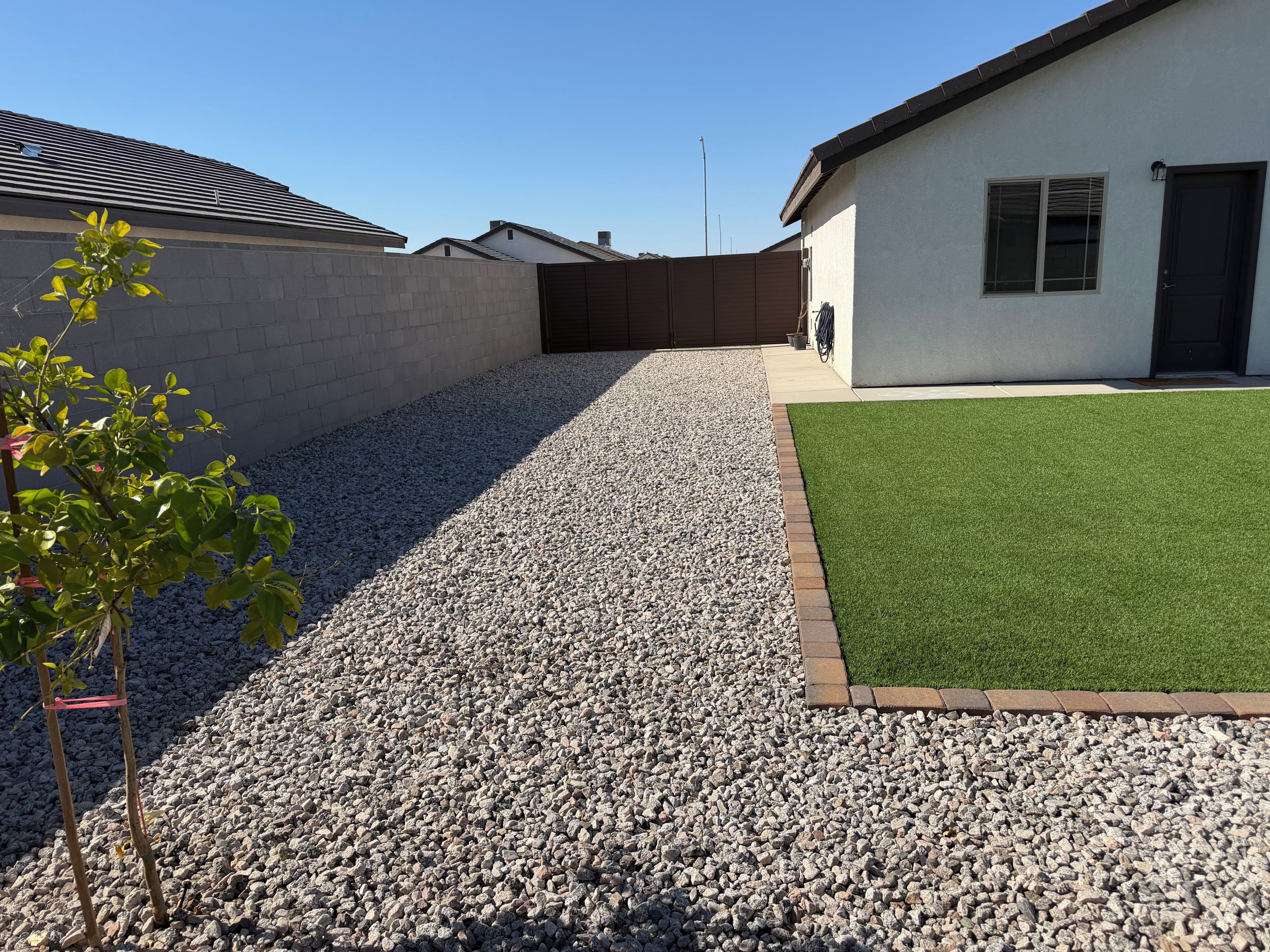 A residential area with a gravel driveway, a green lawn, and a white building with a brown roof.