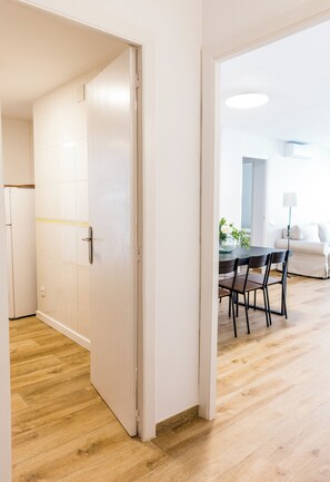 Un couloir au plancher de bois menant à une salle à manger avec une table et des chaises.