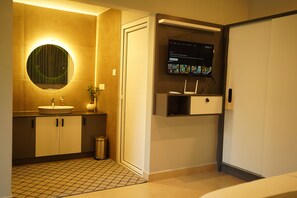 A modern bathroom with a sink, mirror, and a mounted TV displaying a movie selection.