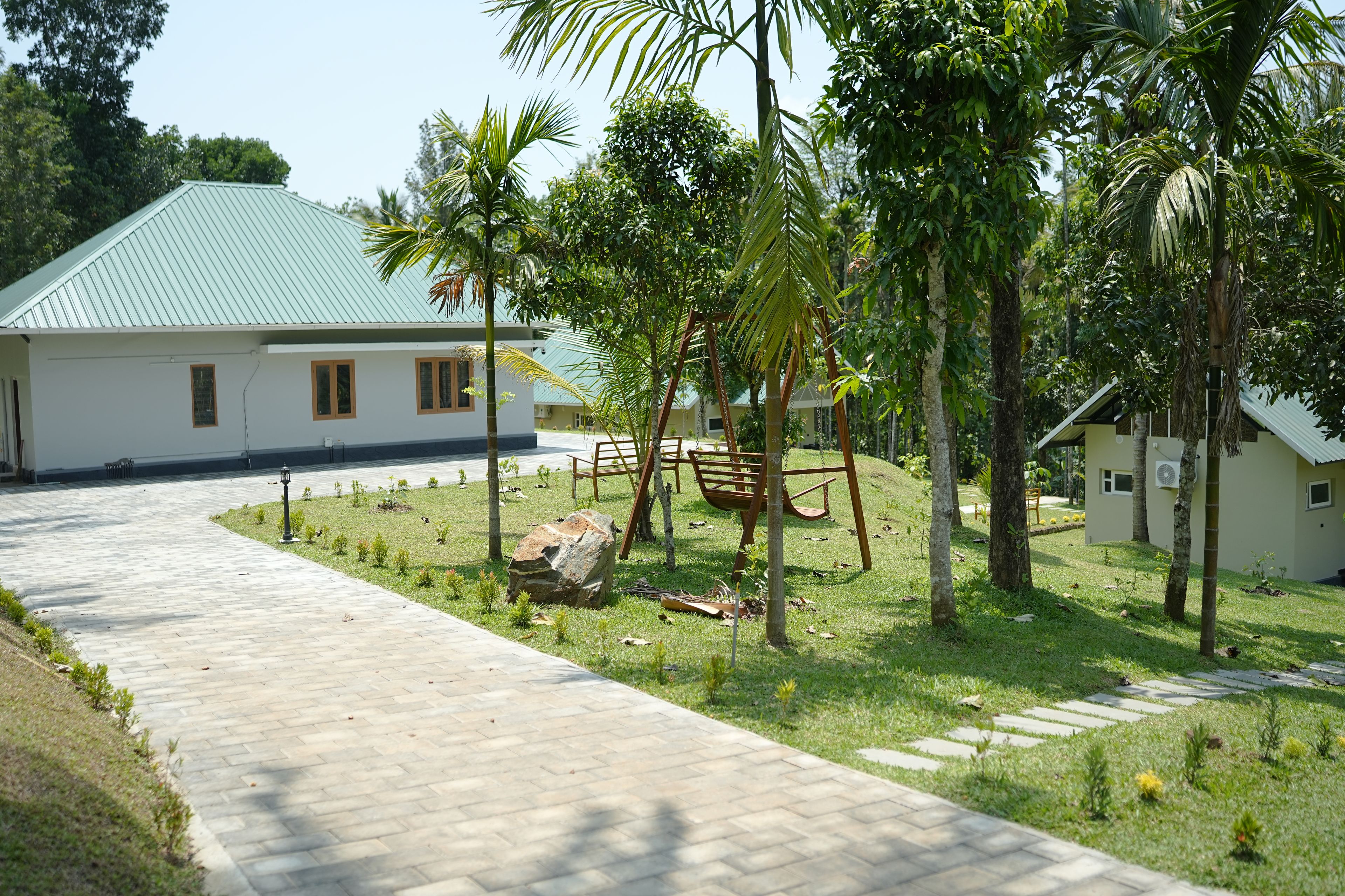 A pathway leading to a building with a green roof, surrounded by a well-maintained lawn and palm trees.