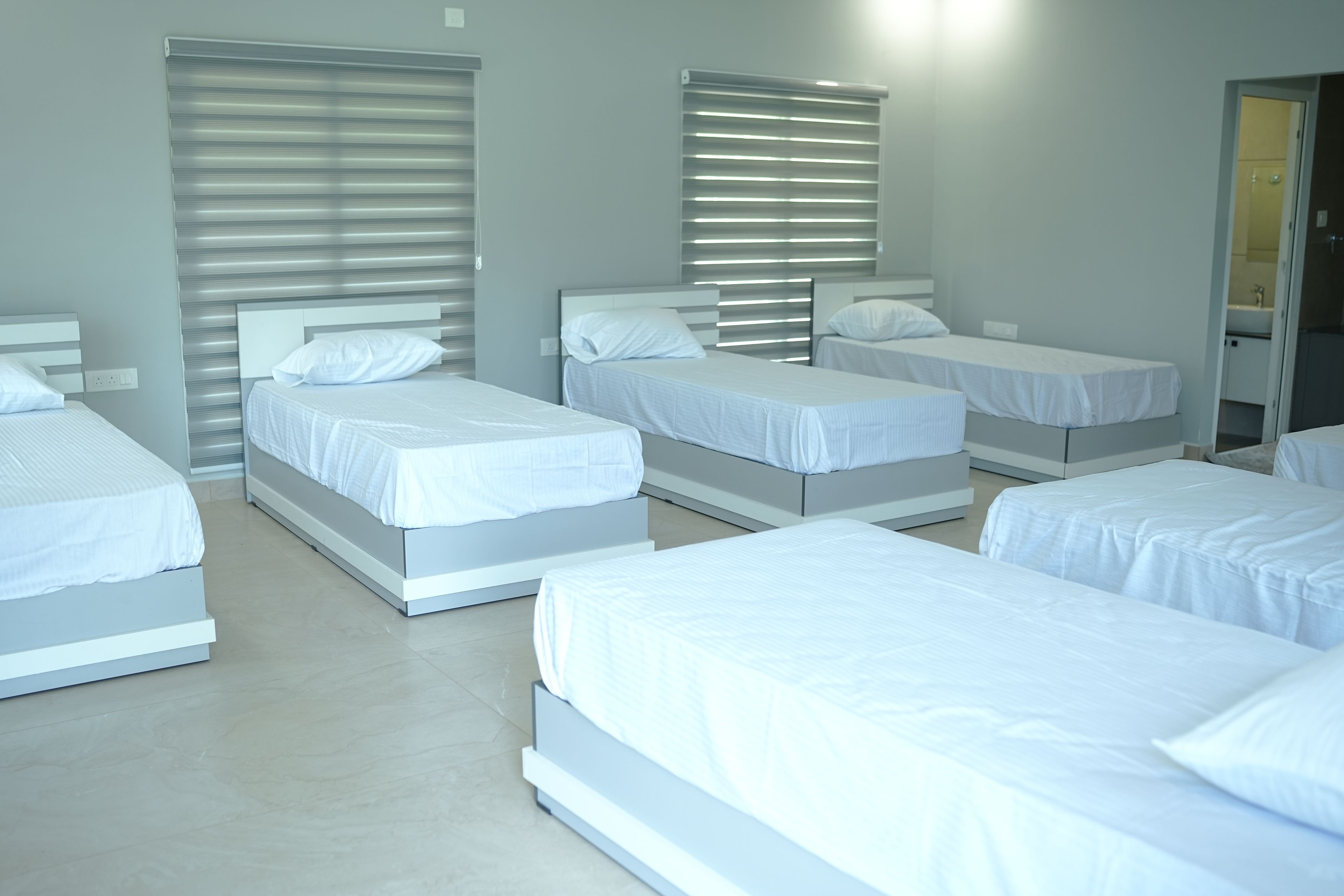 Habitación de hotel con varias camas dispuestas en fila, cada una con ropa blanca y cabeceras.