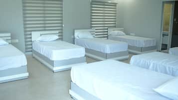 Habitación de hotel con varias camas dispuestas en fila, cada una con ropa blanca y cabeceras.