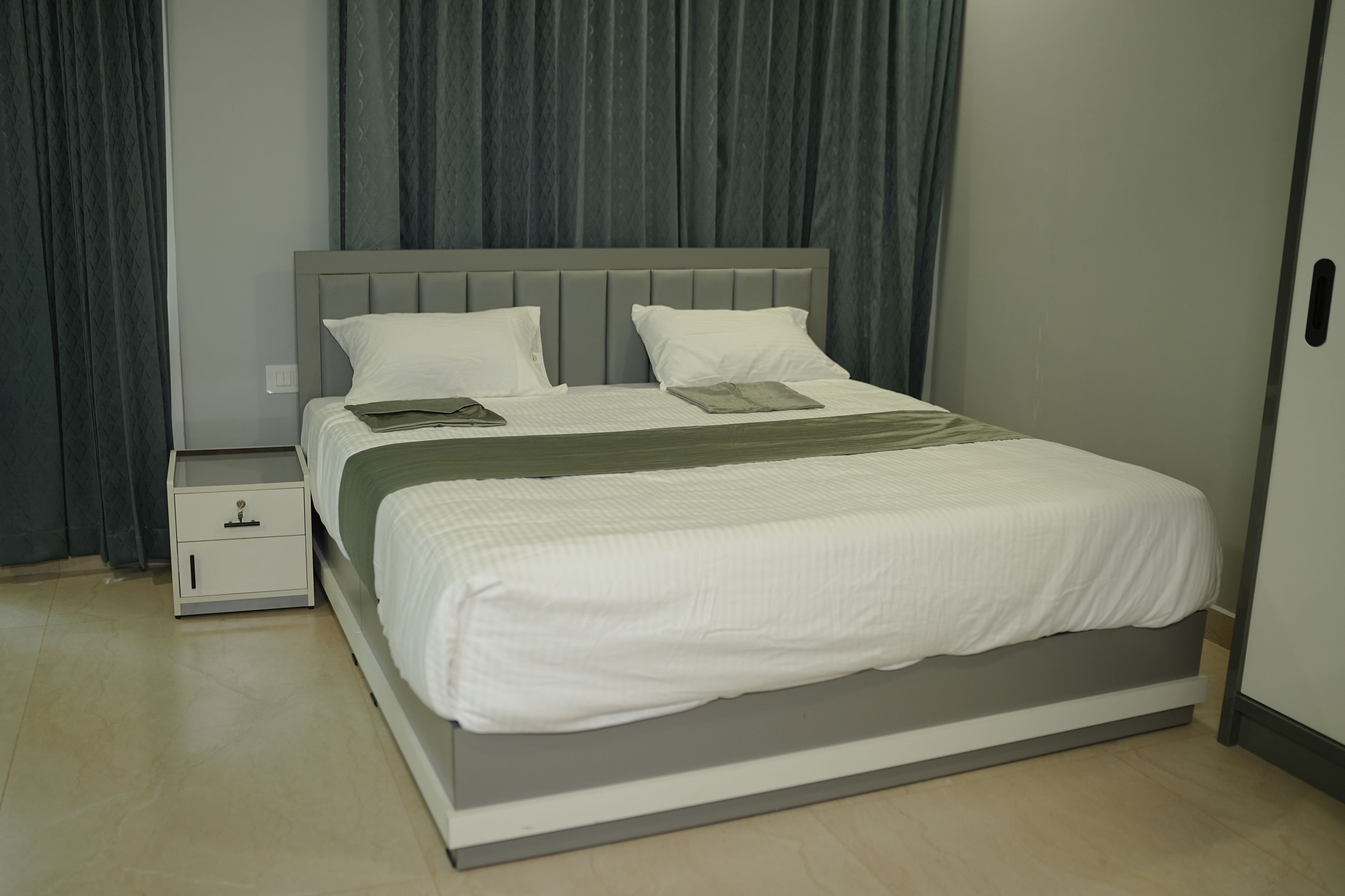 A neatly made bed with a grey headboard, white bedding, and a green throw.