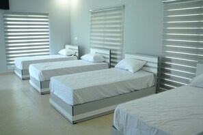 Quarto de hotel com duas camas de solteiro, uma janela grande com cortinas e design moderno.