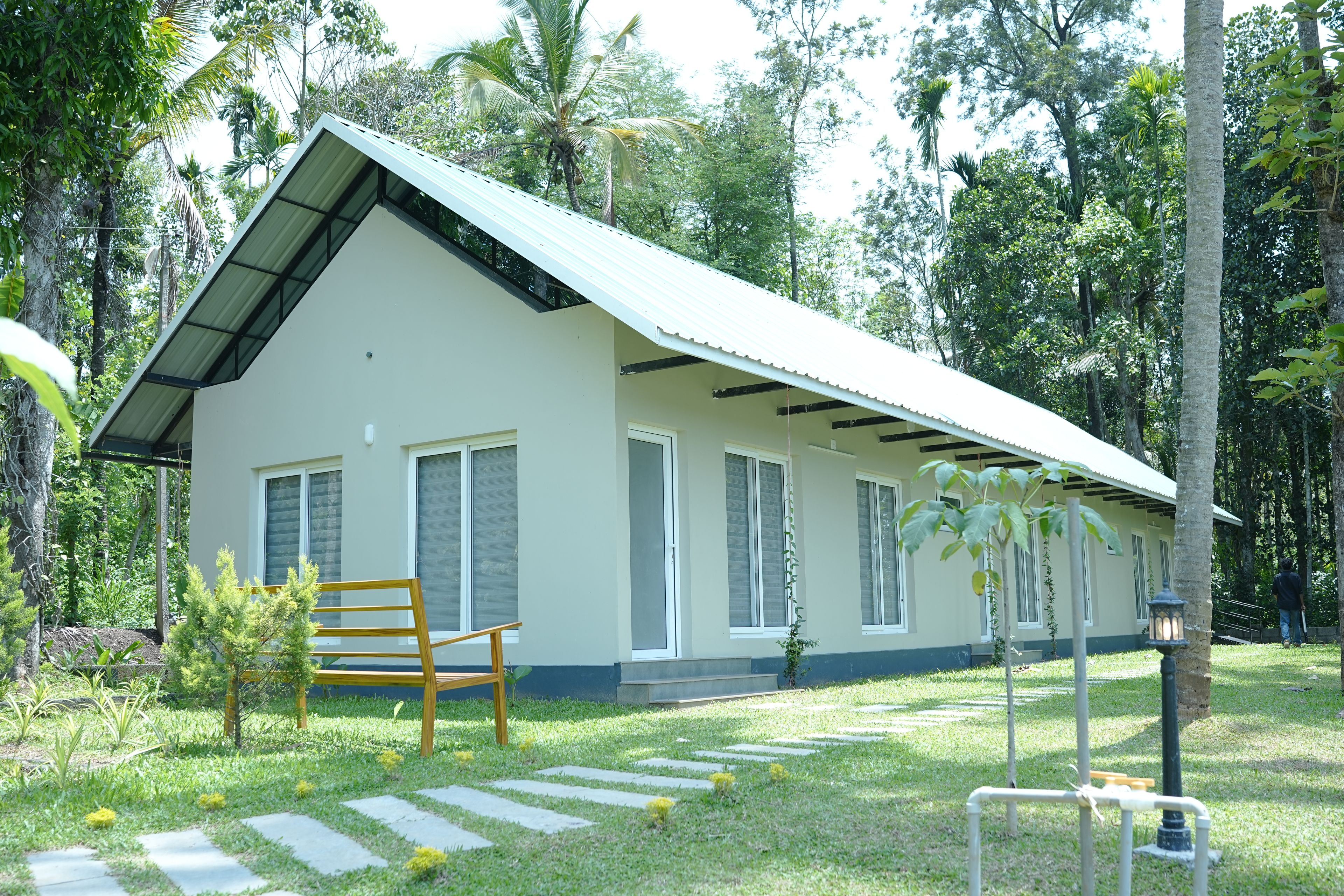 A single-story building with a sloped roof, surrounded by lush greenery and trees.