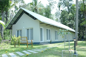 A single-story building with a sloped roof, surrounded by lush greenery and trees. - CLOUDWOOD RESORT (Sulthan Bathery)
