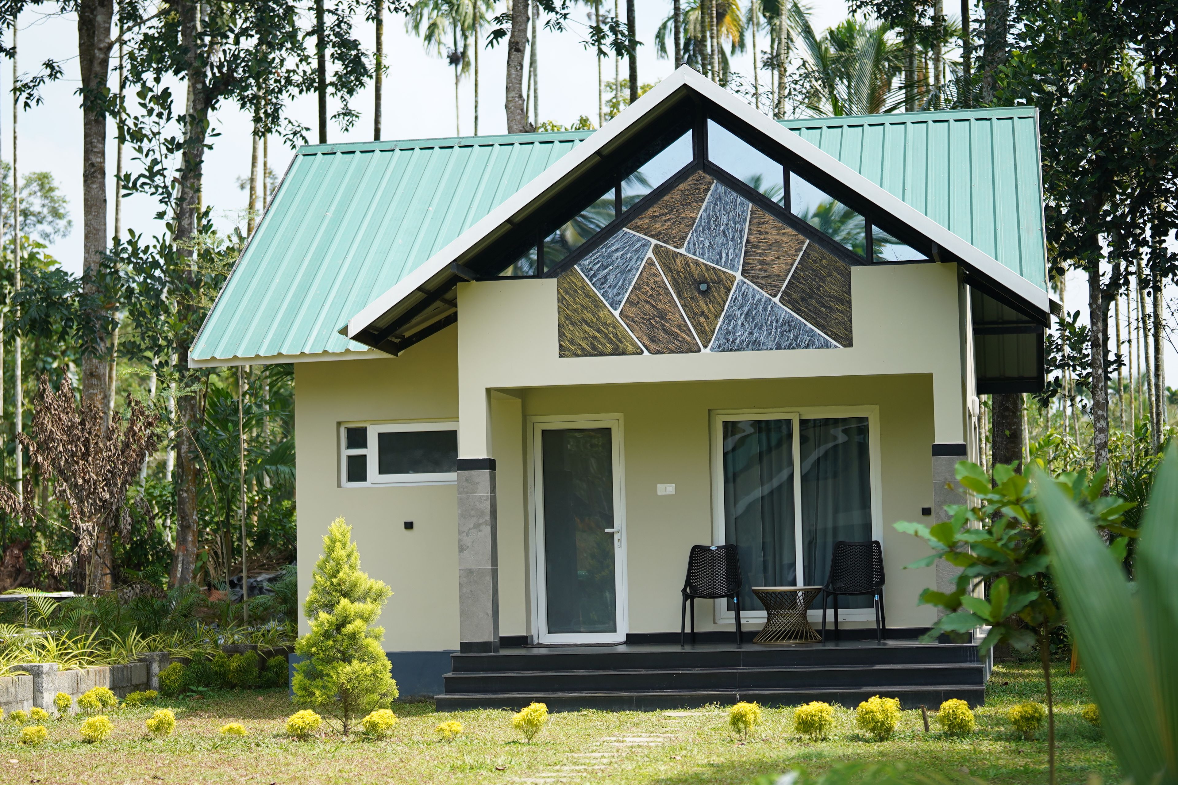 A house with a green roof, a large glass window, and a small porch with two chairs.