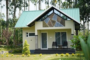 A house with a green roof, a large glass window, and a small porch with two chairs.