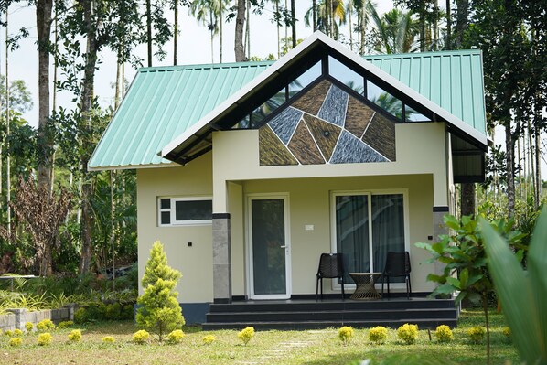 A house with a green roof, a large glass window, and a small porch with two chairs.