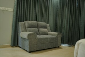 A grey armchair with a cushioned backrest and armrests, positioned in front of a curtain. - CLOUDWOOD RESORT (Sulthan Bathery)