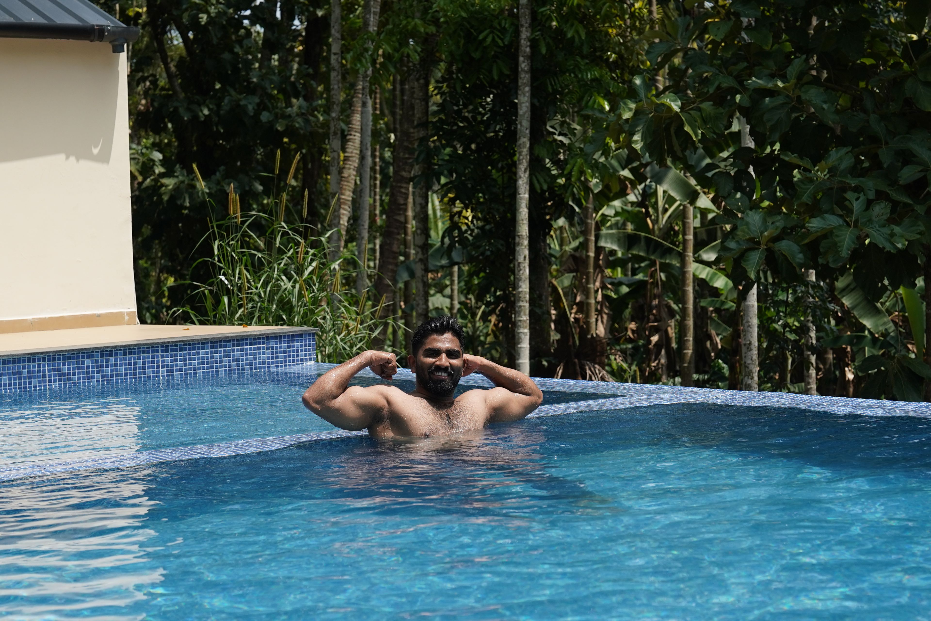 Una persona en una piscina con borde de azulejos, rodeada de follaje.