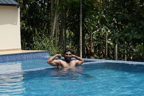 A person in a swimming pool with a tiled edge, surrounded by greenery.