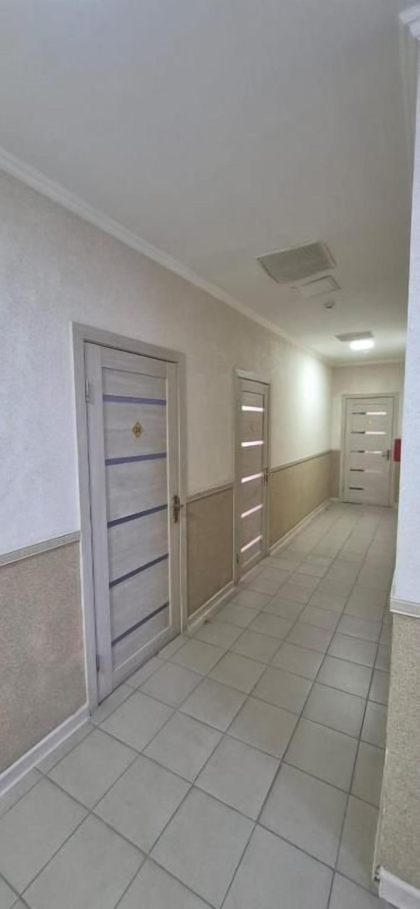 A corridor with doors, a tiled floor, and a ceiling light.