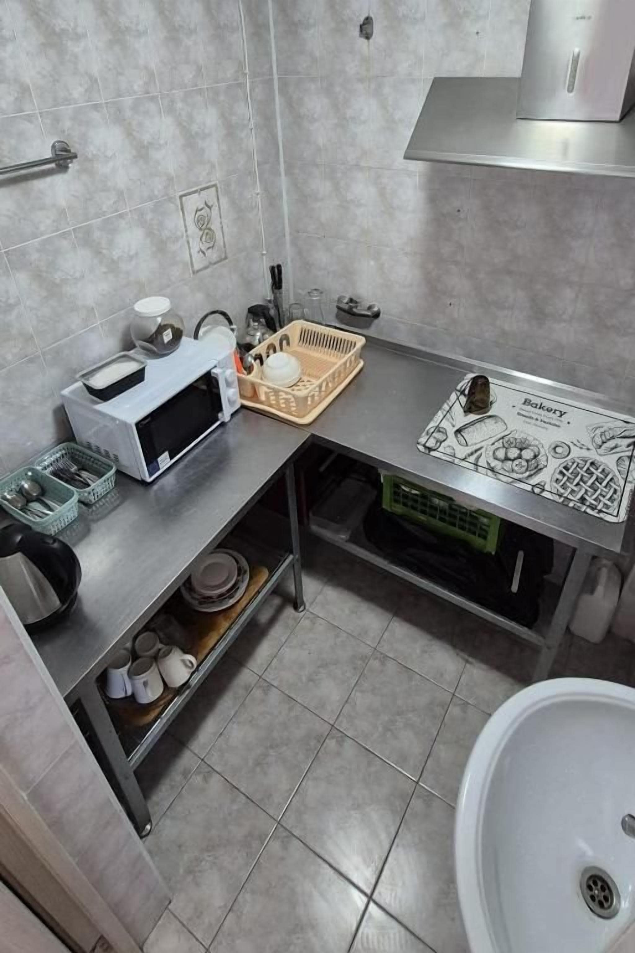 A compact kitchen with a microwave, tea kettle, and a bread basket on the counter.