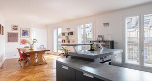 Una cocina moderna con una isla central, mesa de comedor de madera y ventanas grandes.
