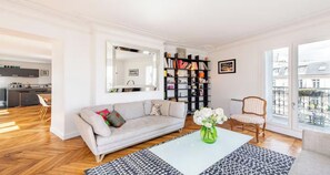 A living room with a sofa, a coffee table, a bookshelf, and a chair. - YOUR PARISIAN HOME AWAY FROM HOME SAINT LAZARE - RUE CLAPEYRON (Paris)