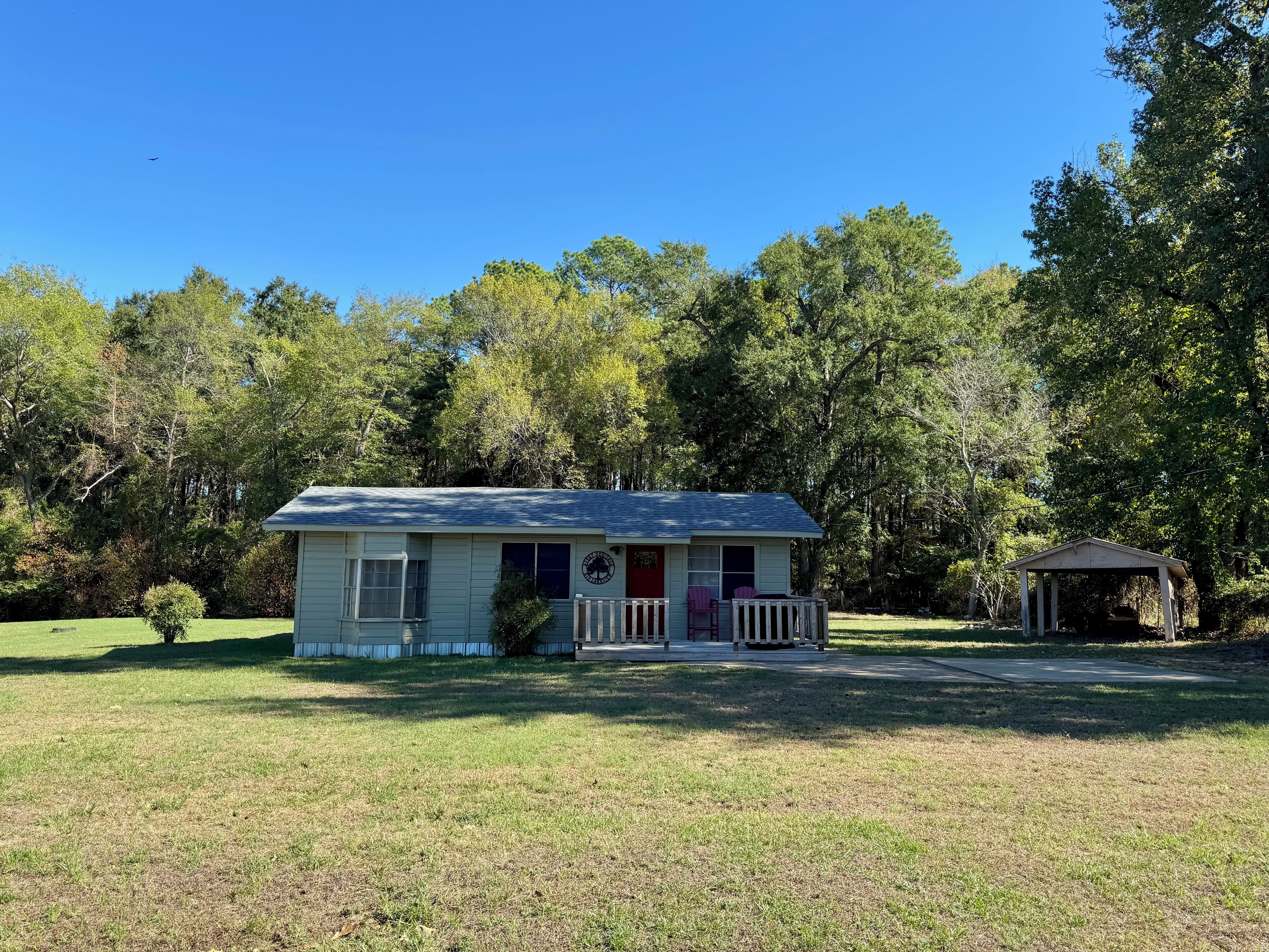 A small house with a porch and a small shed in a grassy area with trees in the background.