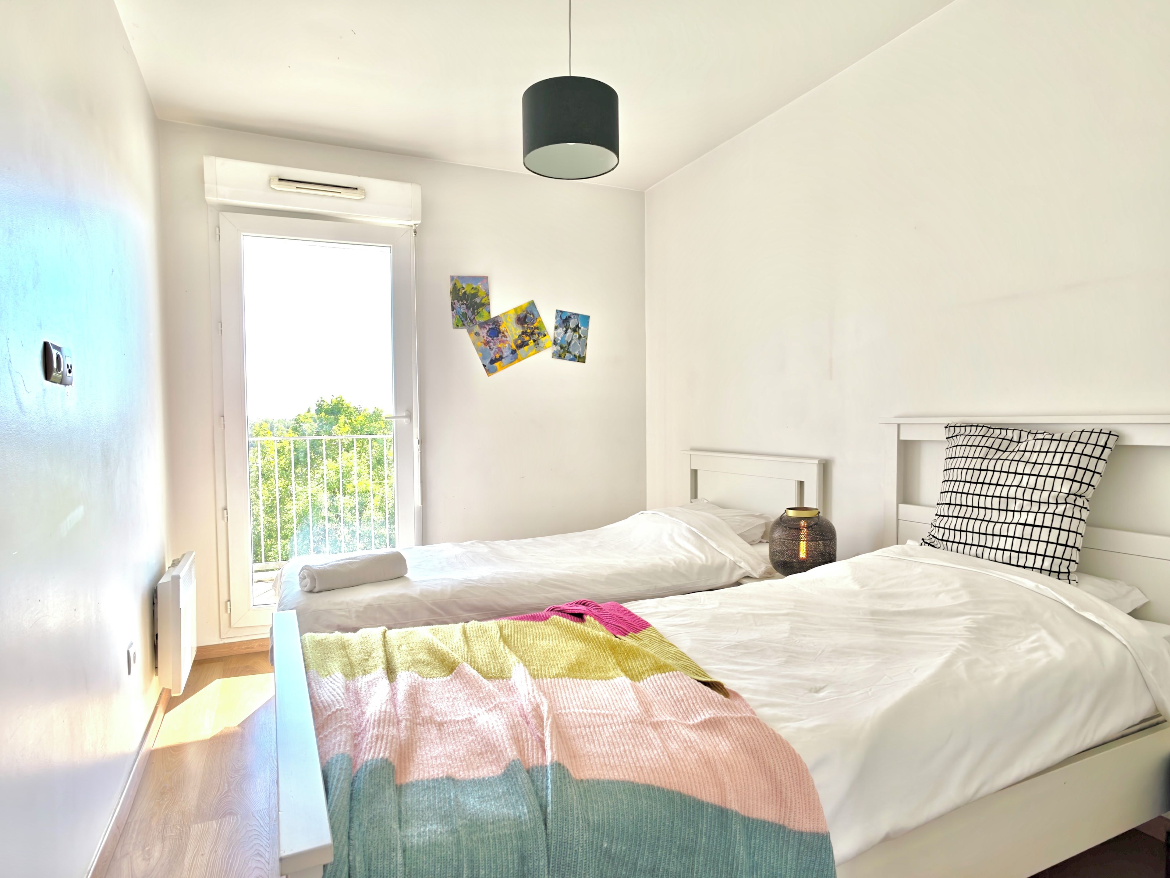 A bedroom with two beds, a window, and a hanging light fixture.