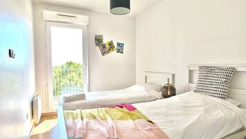 A bedroom with two beds, a window, and a hanging light fixture.