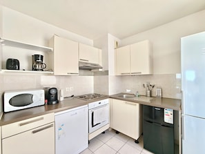 Una cucina moderna con mobili bianchi, forno a microonde integrato, macchina da caffè, lavastoviglie, forno, lavello e frigorifero.
