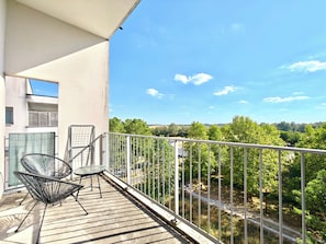 A balcony with a view of a road and greenery, a metal chair, and a table. - New Listing (Montévrain)