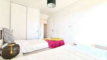 A bedroom with two beds, a bedside lamp, a wardrobe, and a door leading to another room.