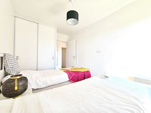 Una camera da letto con due letti, una lampada da comodino, un armadio e una porta che dà su un'altra stanza.