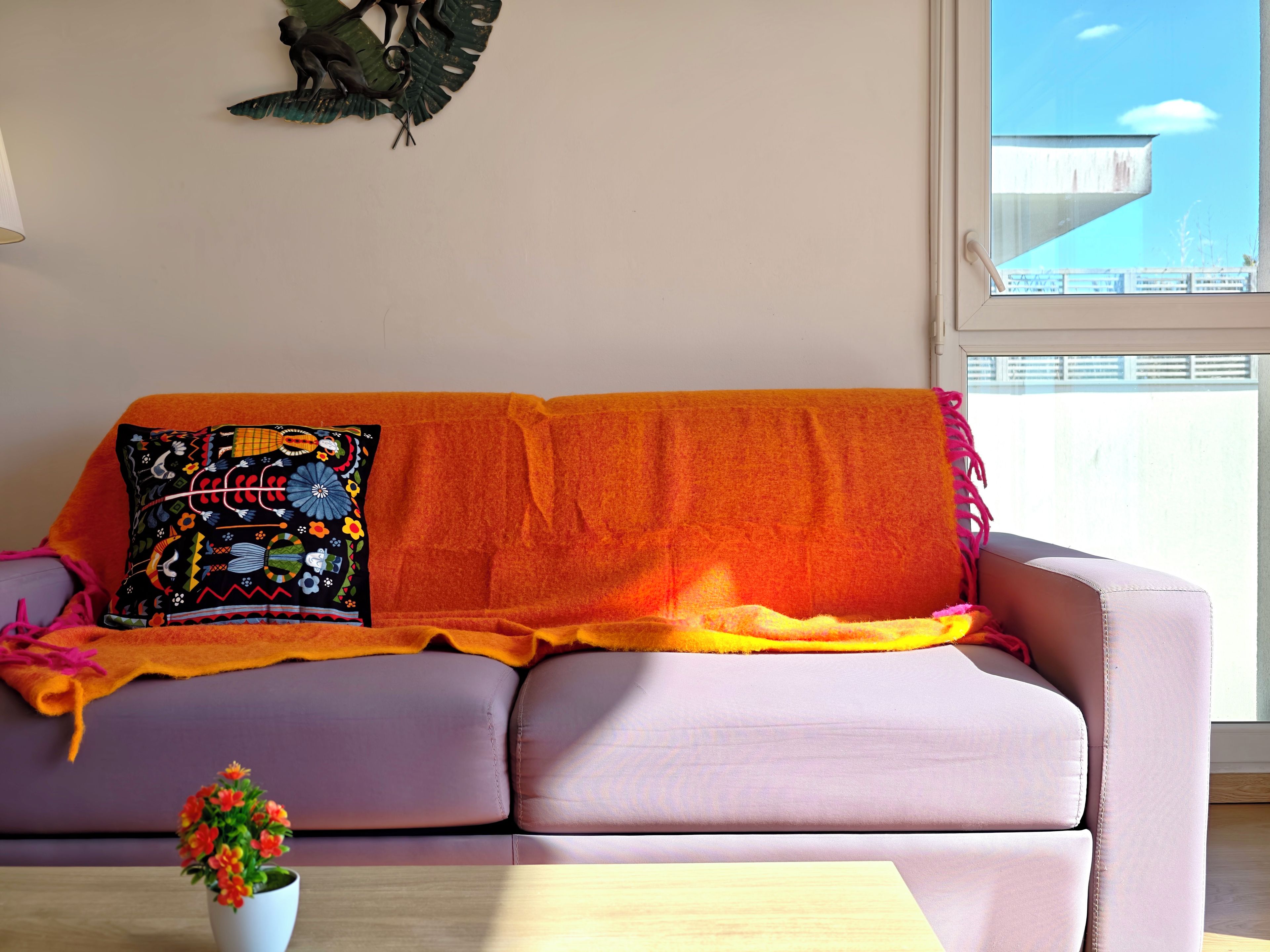 A room with a purple sofa, a decorative pillow, a small potted plant, and a window with a view of a building.