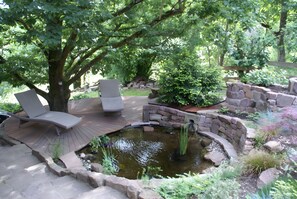 Un jardín con estanque, zona de estar y muros de piedra.