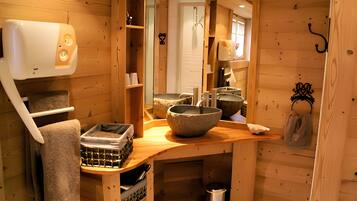 Een houten cabin met een houten bankje, een stenen wasbak en een handdoekhouder.