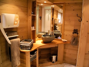 Interior de una cabaña de madera con un banco, una pila de piedra y un perchero.