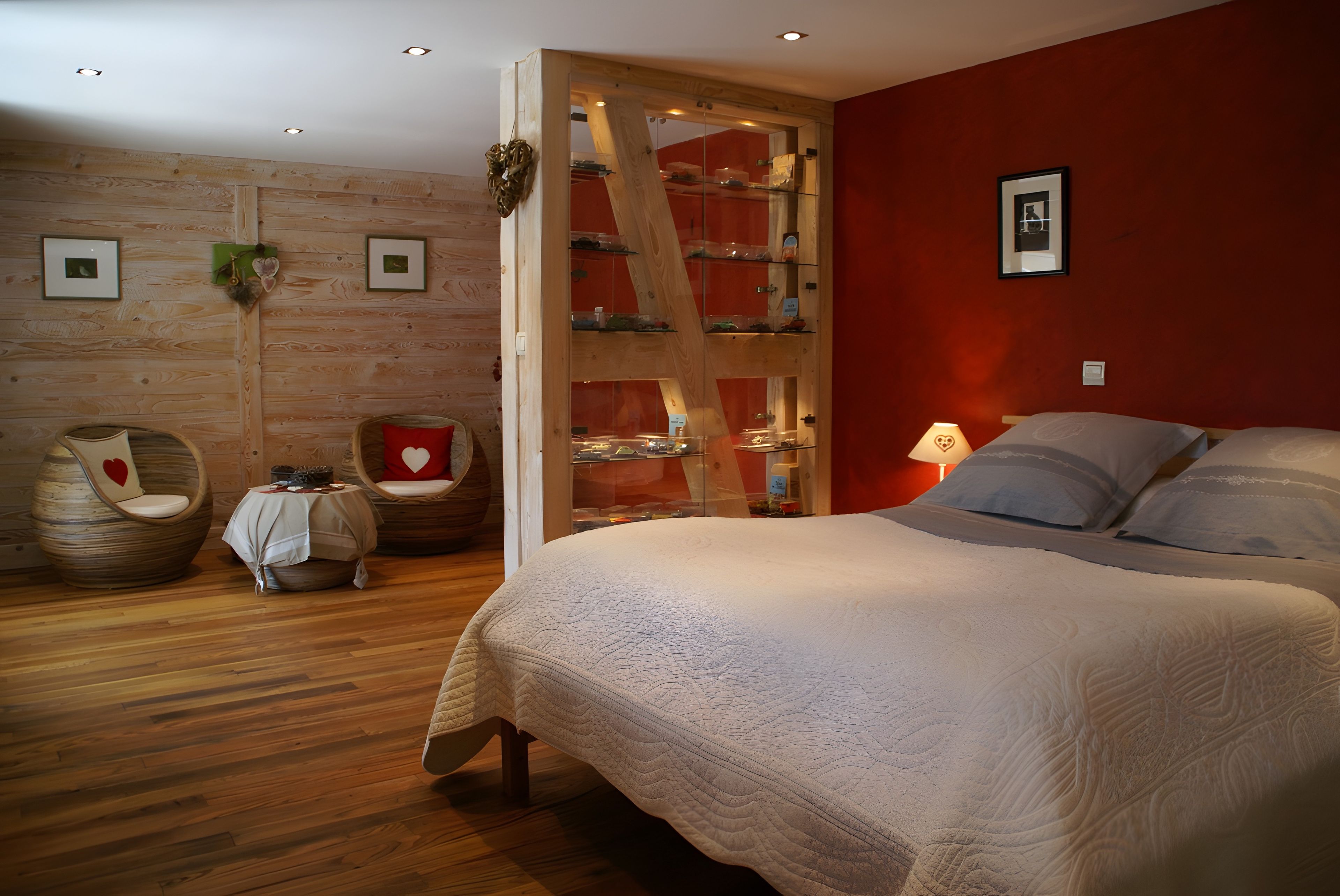 Een slaapkamer met een groot bed, een houten garderobe, een stoel met een hartvormig kussen en een kleine tafel met een decoratie in de vorm van een hart.