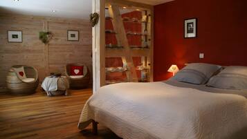 Een slaapkamer met een groot bed, een houten garderobe, een stoel met een hartvormig kussen en een kleine tafel met een decoratie in de vorm van een hart.