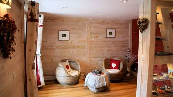 Een kamer met houten wanden, twee ronde stoelen met hartvormige kussens, een bijzettafeltje en wanddecoratie in lijsten.