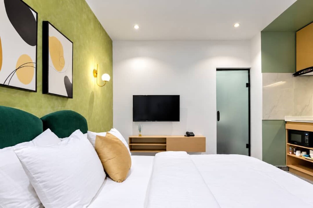 Una habitación de hotel moderna con una cama grande, un televisor de pantalla plana, una mesa consola de madera y una pared verde decorativa.