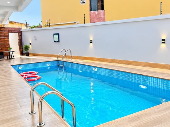 Una piscina interior con superficie de agua cristalina, una terraza de madera que la rodea y una pared con un interruptor de luz y una planta pequeña.