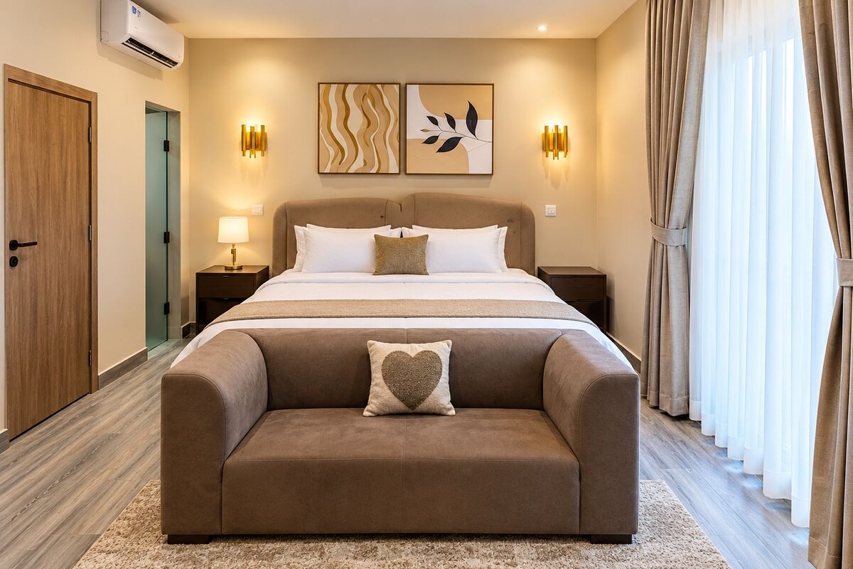 Habitación de hotel con cama, mesitas de noche, sofá, obras de arte y cortinas.