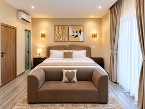 Habitación de hotel con cama, mesitas de noche, sofá, obras de arte y cortinas.