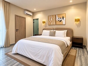 Habitación de hotel con una cama grande, dos mesitas de noche, unidad de aire acondicionado e iluminación empotrada.