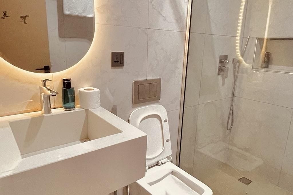 Un baño con un espejo grande, un lavabo, un inodoro y una zona de ducha con mampara de vidrio.