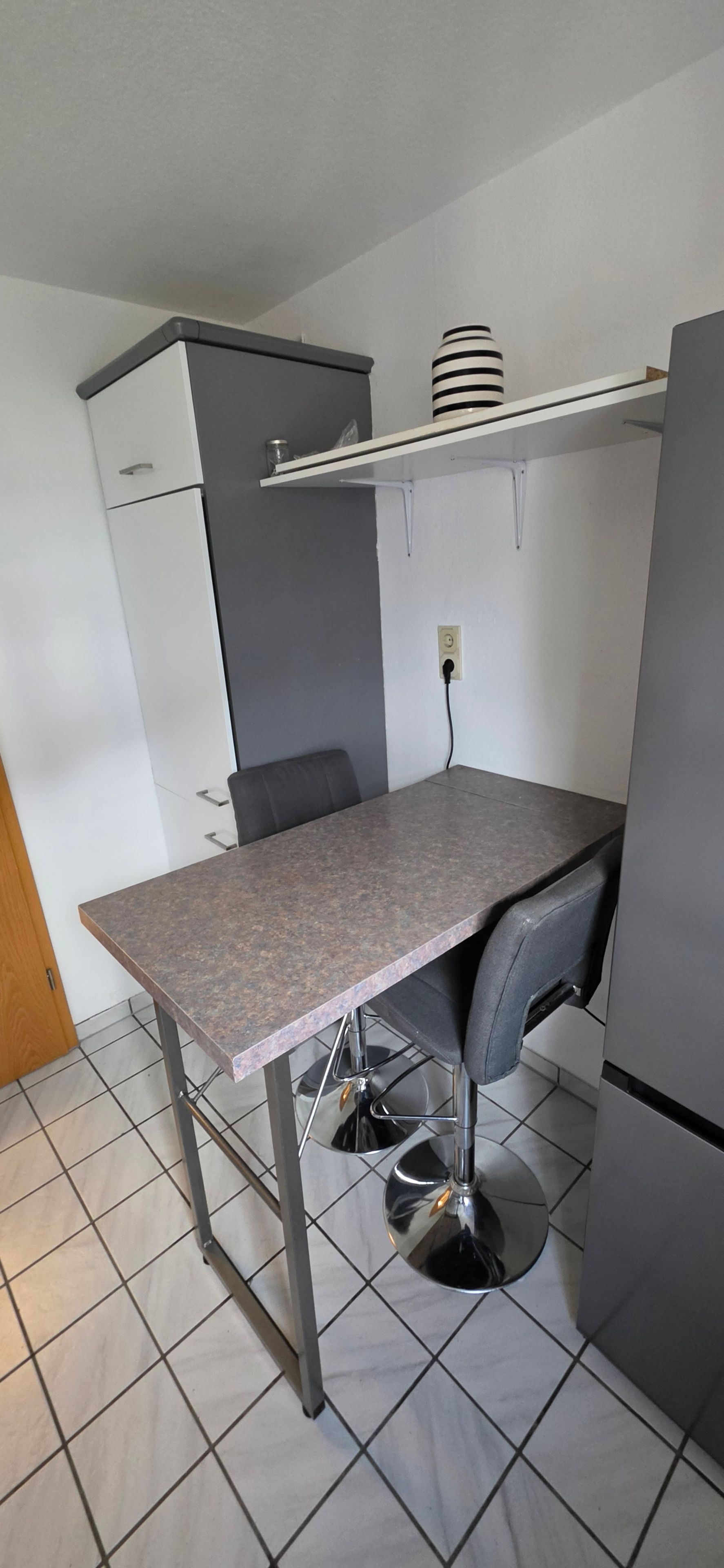 Eine kleine Küchenzeile mit Arbeitsplatte, Stuhl und Kühlschrank.