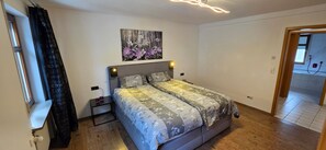 A bedroom with a bed, a nightstand, a wall-mounted light, and a painting above the bed.
