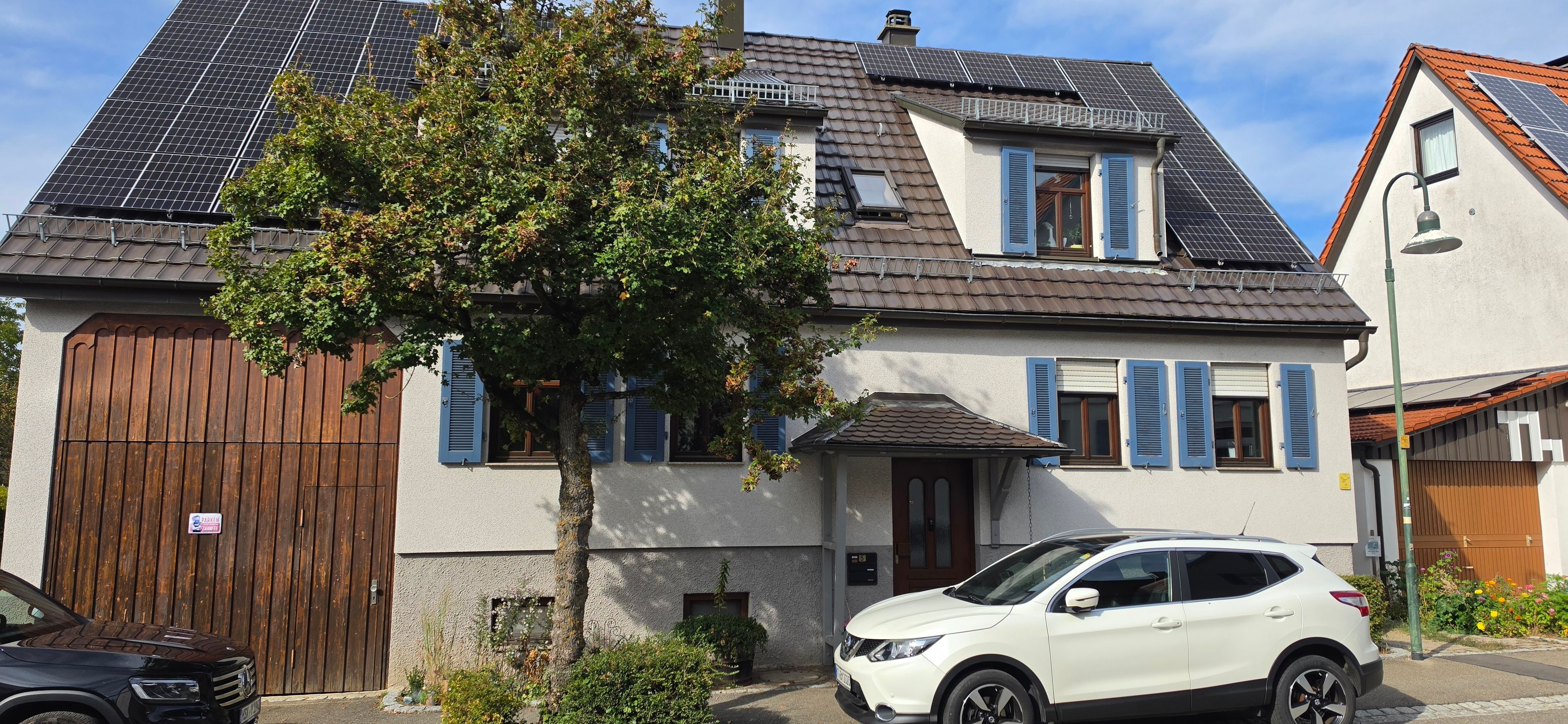 Ein Wohngebäude mit geneigtem Dach, einem Holztor und einem weißen Auto vor der Fassade.