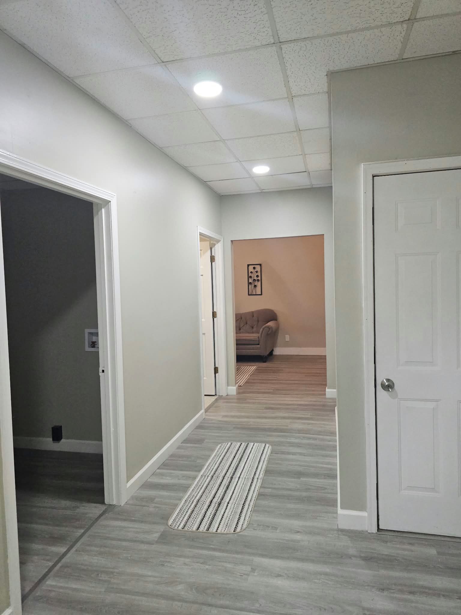 A hallway with a door on the right, a rug on the floor, and a couch in the background.